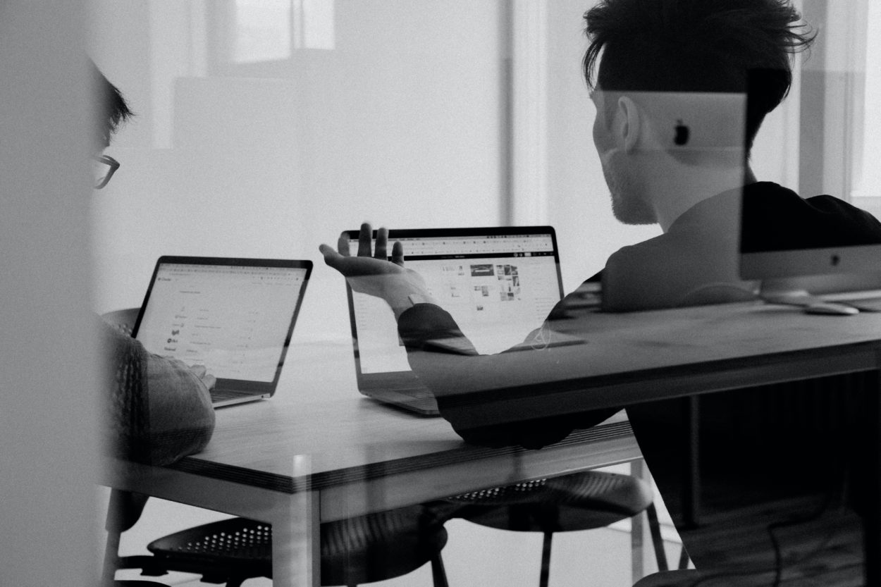 A black and white photo of two people looking at laptops in a conference room having a discussion
