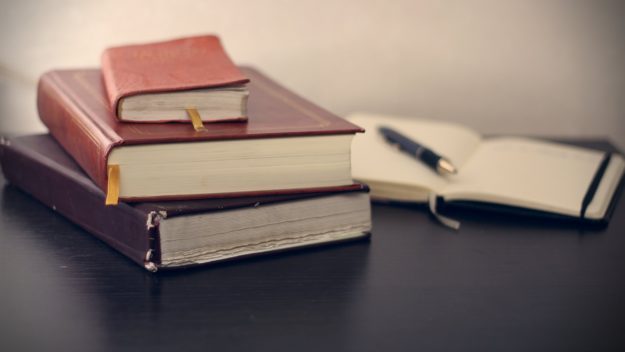 A stack of three leather bound notebooks with a pen and open notebook behind
