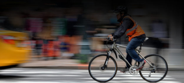 A person wearing an orange vest riding a bicycle on a busy city street