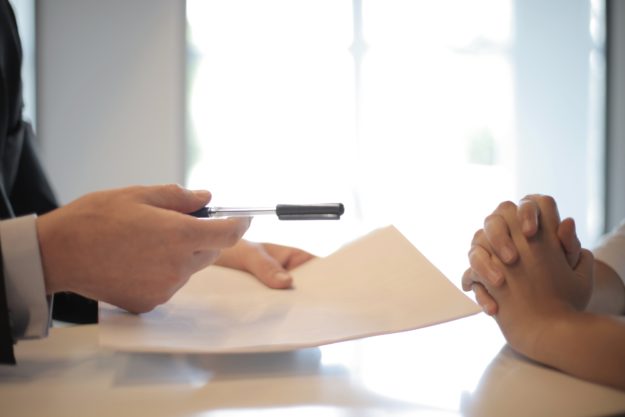Person handing another person a contract and a pen to sign